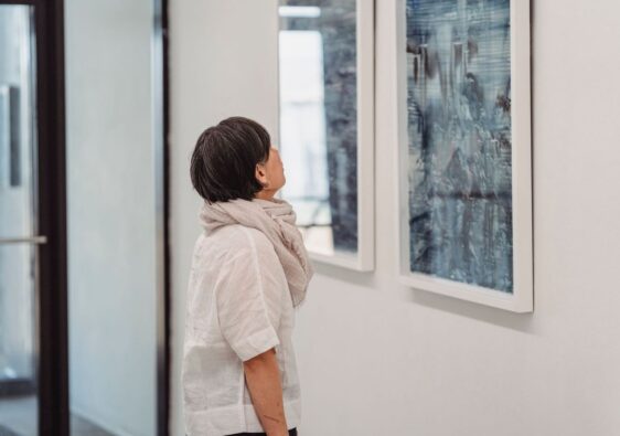 Frau betrachtet konzentriert ein gerahmtes Kunstwerk im Ausstellungsraum